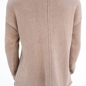 May include: A beige knitted sweater with a wide neckline and long sleeves. The back of the sweater has a vertical seam down the centre. The bottom hem has a scalloped edge. The sweater is made of a soft, textured knit fabric.