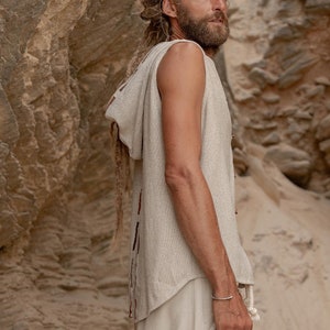 May include: A sleeveless hooded top with a light brown color and a frayed hem. The top is made of a soft, textured fabric and has a relaxed fit. The model is wearing the top with a pair of light brown pants.