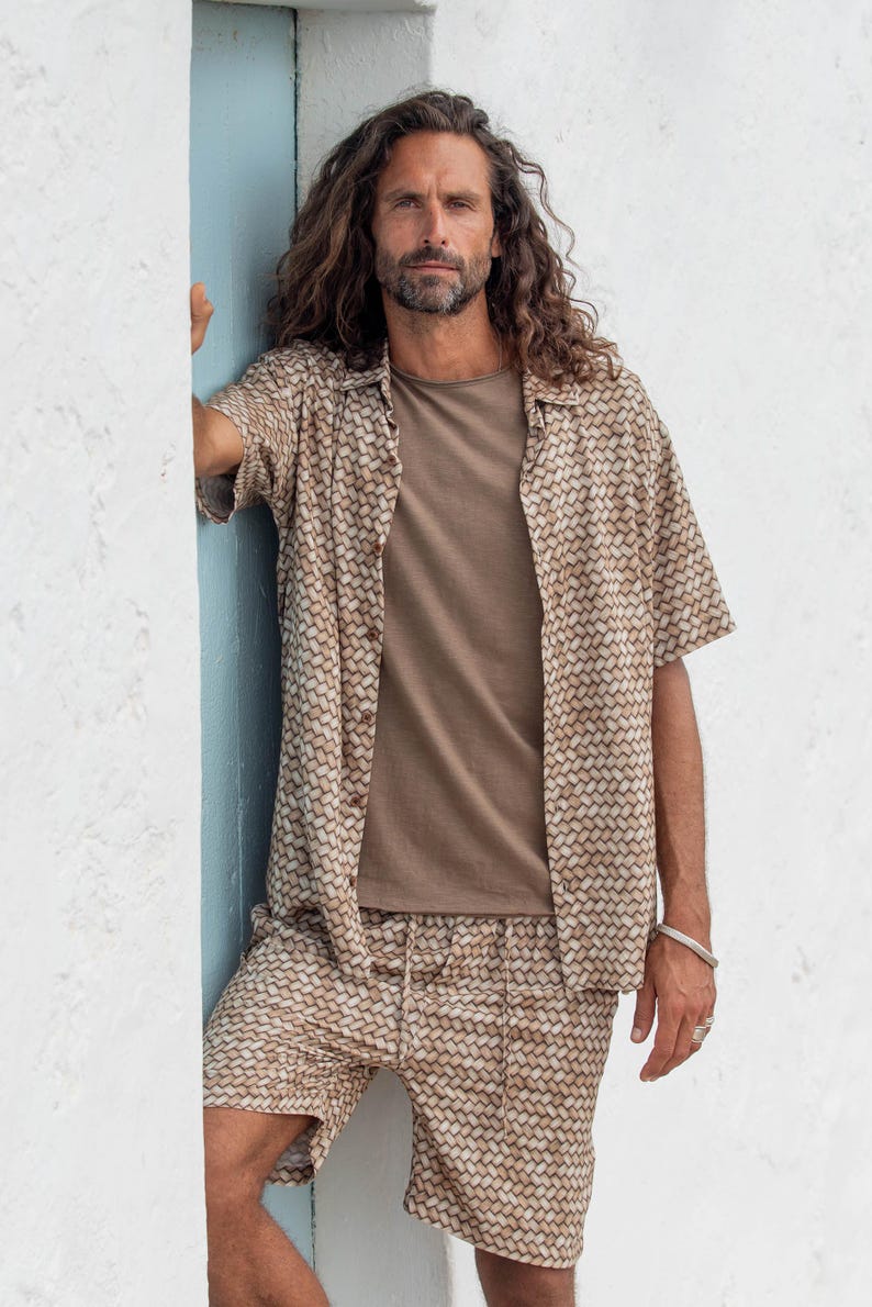 May include: A matching beige shirt and shorts set with a woven pattern. The short-sleeved shirt is buttoned and worn over a solid brown t-shirt. The shorts have a drawstring waist. The outfit is casual and suitable for warm weather.