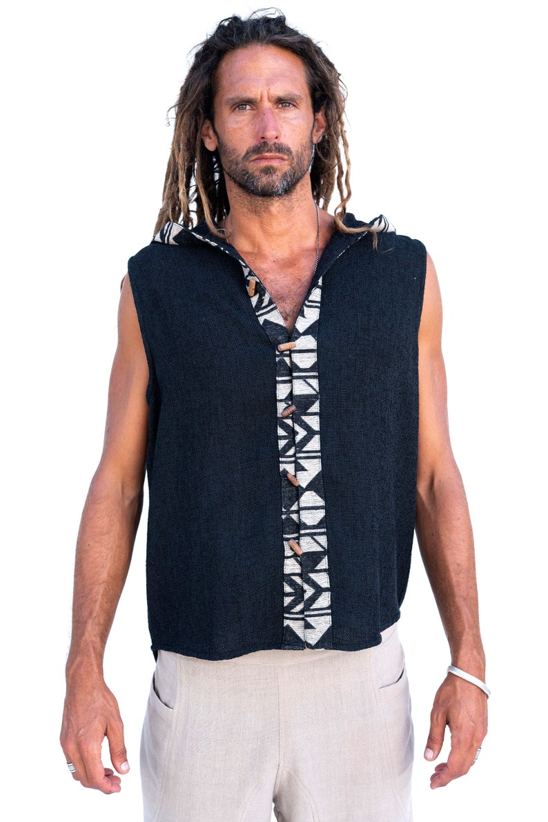 Op de afbeelding: Een mouwloos hooded shirt met een zwarte gebreide stof en een wit en zwart geometrisch patroon aan de voorkant. Het shirt heeft houten knopen.