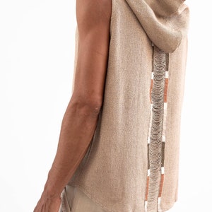 May include: A sleeveless hooded top with a brown and white trim along the back. The top is made of a soft, textured fabric.