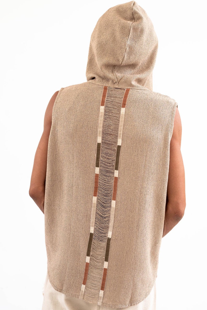 May include: A sleeveless hooded top with a brown, beige, and white striped design down the back. The top is made of a textured fabric.