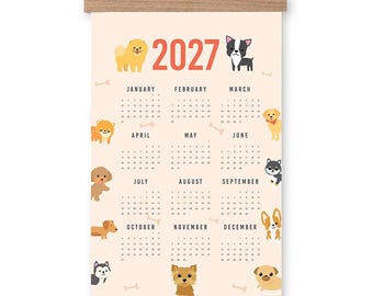 Puede incluir: Un calendario de pared para 2027 con un fondo color melocotón claro e ilustraciones de varias razas de perros. El calendario se sujeta con dos listones de madera horizontales en la parte superior e inferior, con un cordel marrón para colgarlo.