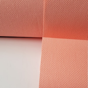 May include: A roll of peach-coloured Aida cloth, a type of fabric used for cross-stitch embroidery.