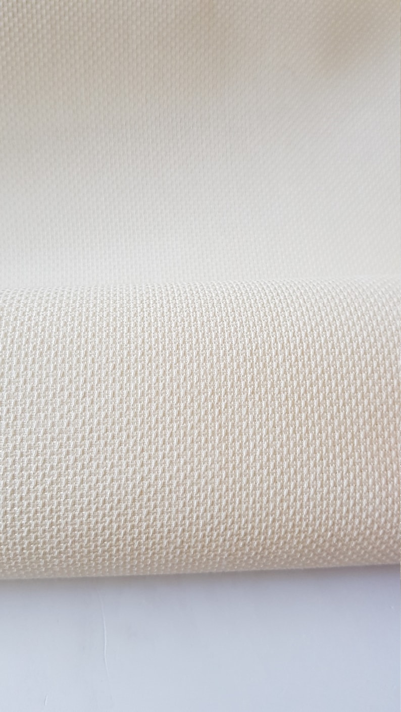 May include: A close-up of a cream-colored fabric with a woven texture. The fabric is folded in half, showing the texture of the weave.