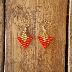 May include: A pair of geometric triangle earrings with a gold and orange color scheme. The earrings are made of small beads and have a simple, modern design.