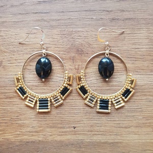 May include: A pair of gold hoop earrings with black bead accents and a black oval gemstone hanging from each hoop.