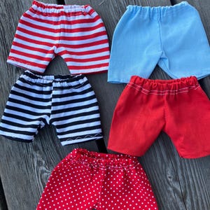 May include: Five pairs of shorts in different patterns. The shorts are red with white stripes, black with white stripes, light blue, red with white polka dots, and red with white stripes.