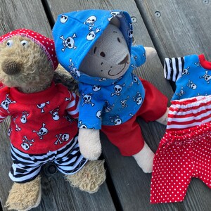 May include: Two teddy bears dressed in pirate-themed outfits. One bear is wearing a blue hoodie with a skull and crossbones pattern, red trousers, and a red and white striped bandana. The other bear is wearing a red shirt with a skull and crossbones pattern, black and white striped trousers, and a red and white polka dot bandana.