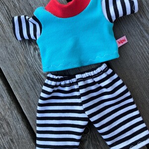 May include: A blue and red striped shirt with black and white striped sleeves and matching black and white striped pants. The shirt has a red collar and the tag says "kipu".