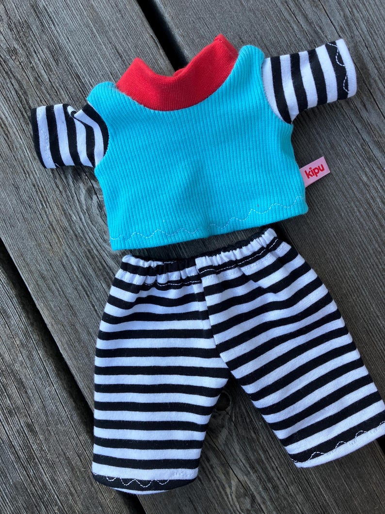 May include: A blue and red striped shirt with black and white striped sleeves and matching black and white striped pants. The shirt has a red collar and the tag says "kipu".