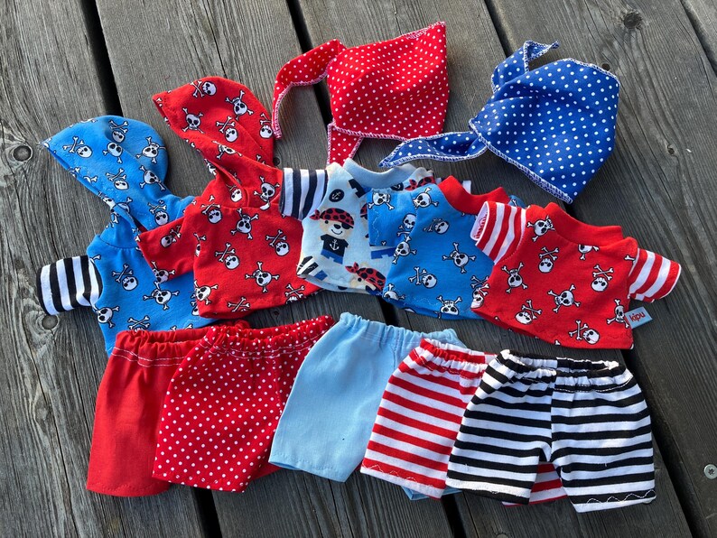 May include: A set of seven handmade doll clothes featuring a pirate theme. The set includes a red and white polka dot skirt, a blue and white striped skirt, a red and white striped skirt, a blue and white striped shirt, a red and white striped shirt, a red shirt with a skull and crossbones pattern, and a blue shirt with a skull and crossbones pattern.
