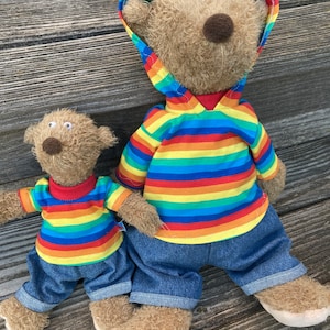 Könnte beinhalten: Zwei Plüschbären, die regenbogenfarbene gestreifte Hemden und blaue Jeanshosen tragen. Der größere Bär trägt ein regenbogenfarbenes gestreiftes Kapuzen-Sweatshirt.