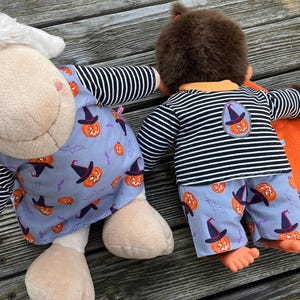 May include: Two plush toys dressed in Halloween-themed outfits. One is a sheep wearing a light blue dress with pumpkin and witch hat print, and black and white striped sleeves. The other is a monkey in matching pajamas.