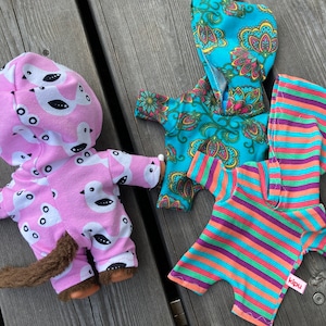 May include: Three hooded baby doll outfits. One is pink with white bird prints, one is turquoise with a paisley pattern, and one is striped in orange, purple, and turquoise.