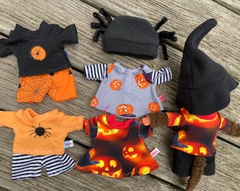 May include: A collection of doll clothing featuring Halloween themes, including a black spider hat, two t-shirts with spider motifs, two dresses with pumpkin prints, and a black pointed hat. The garments display orange, black, and grey colors.