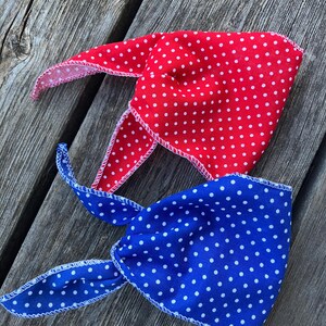 May include: Two fabric bandanas with white polka dots on a red and blue background. The bandanas are tied together and laid on a wooden surface.