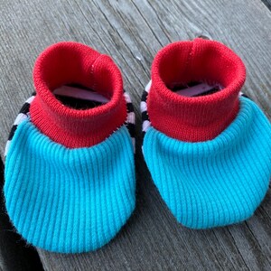 May include: A pair of baby booties with a red, white, and black striped cuff and a turquoise blue body.