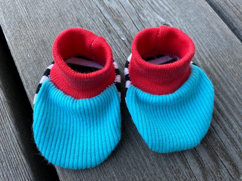 May include: A pair of baby booties with a red, white, and black striped cuff and a turquoise blue body.