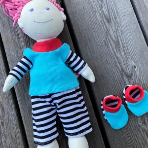 May include: A handmade doll with pink hair, wearing a turquoise shirt with black and white stripes, black and white striped pants, and red and turquoise booties.
