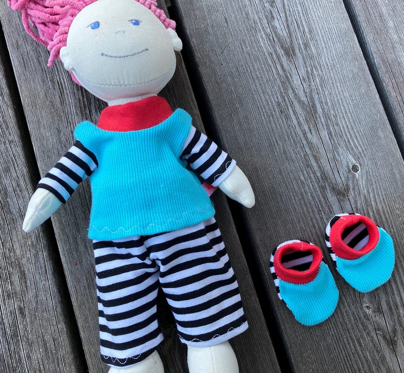 May include: A handmade doll with pink hair, wearing a turquoise shirt with black and white stripes, black and white striped pants, and red and turquoise booties.