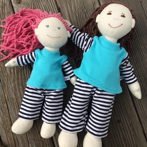May include: Two cloth dolls wearing blue and white striped pajamas. The doll on the left has pink yarn hair and the doll on the right has brown yarn hair.