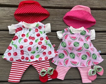 May include: Two doll outfits with a cherry and watermelon print. Each outfit includes a dress, leggings, and a hat. The cherry outfit has red and white striped leggings and a red polka dot hat. The watermelon outfit has pink and white striped leggings and a pink polka dot hat.