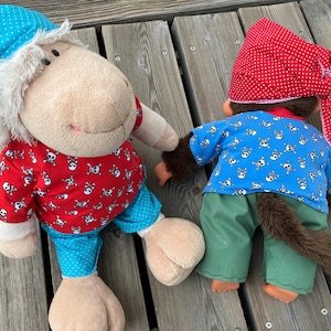 May include: Two soft toys dressed as pirates. One is a sheep wearing a red shirt with skull and crossbones, blue polka dot trousers, and a blue cap. The other is a monkey in a blue skull shirt, green trousers, and a red polka dot bandana.