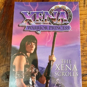 May include: A sealed DVD box set of "Xena: Warrior Princess" with a purple and pink background. The cover features Xena holding a staff, with the title and "The Xena Scrolls" text.