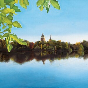 May include: A painting of a lake with a building and a spire in the distance, surrounded by trees. The lake is reflecting the sky and the trees. The painting is framed by a branch of green leaves.