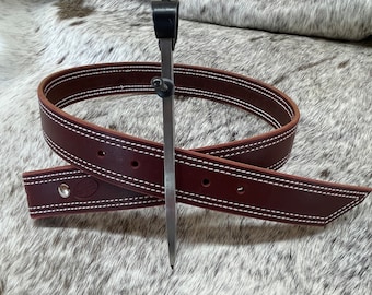May include: A brown leather belt with white stitching and a silver buckle. The belt is folded in half and a metal tool is laying on top of it.