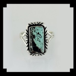 May include: A silver ring featuring a rectangular turquoise stone with black veining. The stone is set in a decorative bezel with a stylized floral design. The ring has a split shank design.