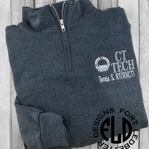 May include: Dark gray quarter-zip sweatshirt with embroidered "CT TECH" text and a medical imaging graphic. The sweatshirt also features the name "Torrie S. RT(R)(CT)" and the "DESIGNS FORT LEDBETTER" logo.