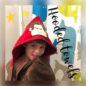 May include: A red hooded towel with a cartoon character embroidered on the hood. The character has brown hair, a red shirt, and a grumpy expression. The towel is being worn by a child. The text "CONNOR" is embroidered below the character.