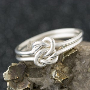 May include: A silver ring with a knot design. The ring is made of two bands of wire that are twisted together to form a knot.