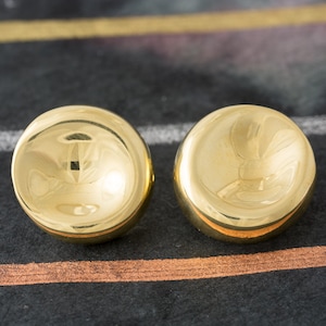 Puede incluir: Un par de pendientes de color dorado en forma de cúpula.