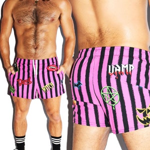 May include: Pink and black striped swim trunks with various graphic patches, including "Devil", "Witch", "Vamp", and a pentagram.