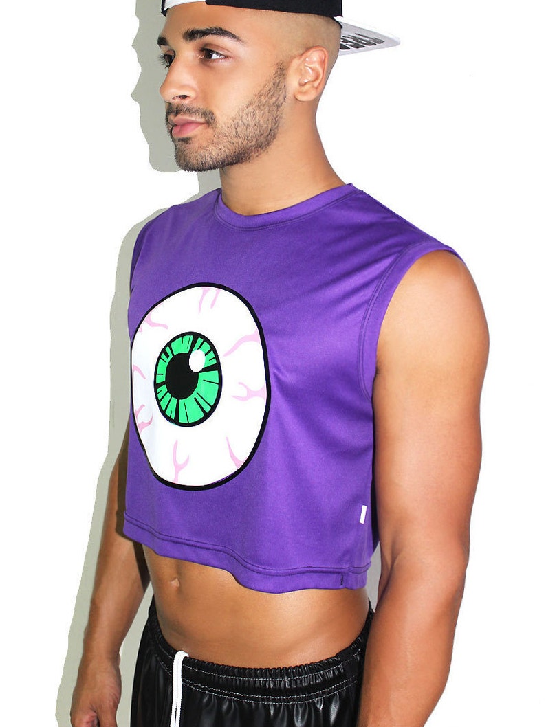 May include: Purple sleeveless crop top with a large white eye graphic with a green iris. The top has a cropped hemline.
