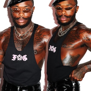 May include: A black sleeveless shirt with a pink "FOG" graphic and a pentagram symbol. The model is wearing a black beret and sunglasses.