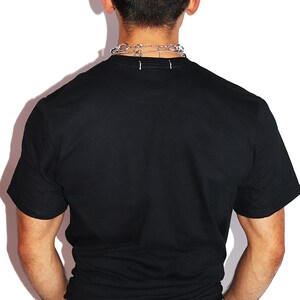 K&ouml;nnte beinhalten: Ein schwarzes T-Shirt mit kurzen &Auml;rmeln und einem Rundhalsausschnitt. Die Person tr&auml;gt eine blaue Jeans.