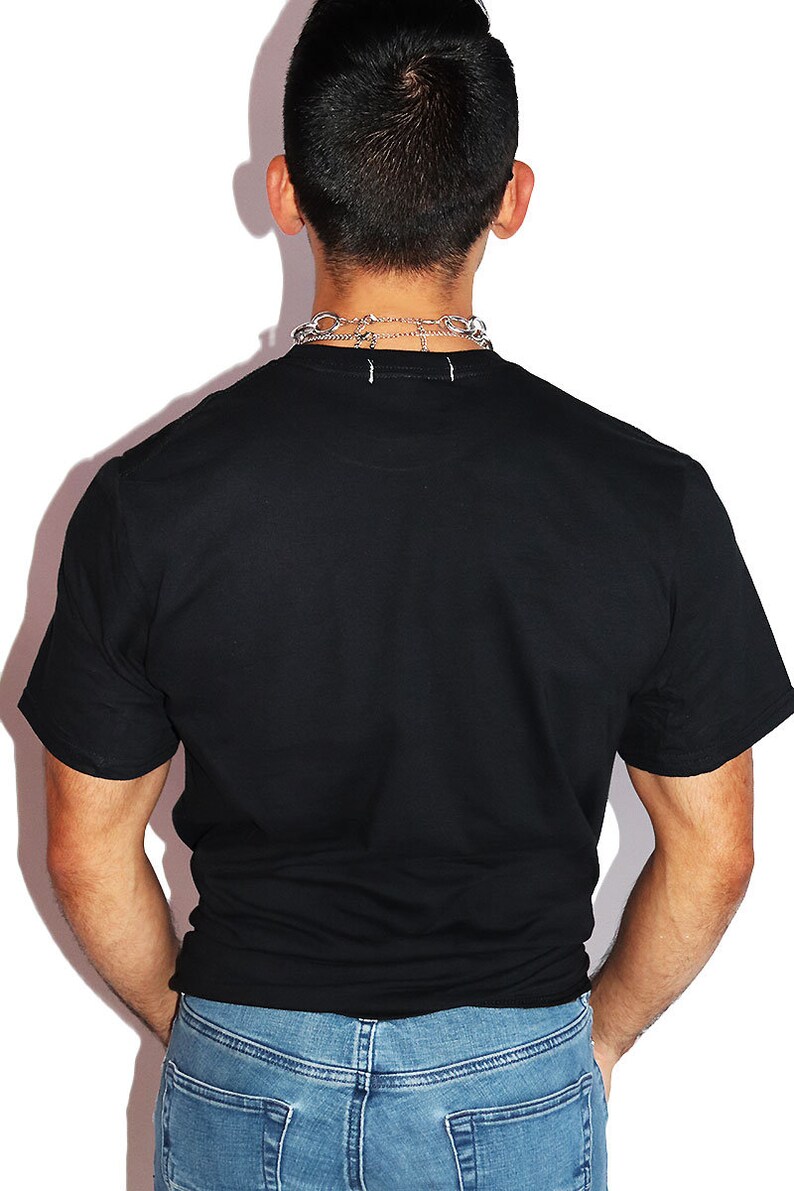 K&ouml;nnte beinhalten: Ein schwarzes T-Shirt mit kurzen &Auml;rmeln und einem Rundhalsausschnitt. Die Person tr&auml;gt eine blaue Jeans.