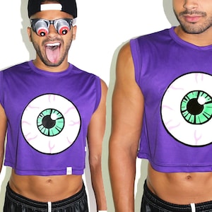 May include: Purple cropped tank top with a large white eye graphic with a green iris and black pupil. The tank top has a sleeveless design.