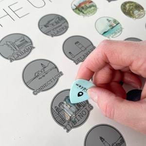 May include: A light blue guitar pick with the word "wayp" and a location icon is held over a gray circle labeled "ILLINOIS" on a white map. The map features illustrations of U.S. states, including "ALABAMA," "ALASKA," and "MAINE."