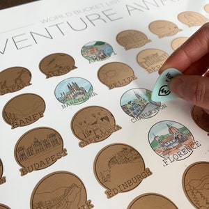 May include: A brown paper world travel bucket list poster with illustrations of various cities and landmarks. The poster has the title "World Bucket List Venture Away" and includes destinations such as Alaska, Amalfi, Amsterdam, Banff, Barcelona, Belize, Budapest, Cappadocia, Charleston, Edinburgh, Florence, and more.