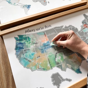May include: A watercolor map of the United States with the states labeled. The map is in a wooden frame and has a white background. The text "places we've been" is written at the top of the map.