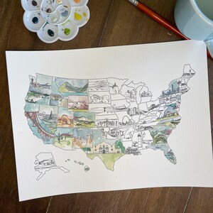 Op de afbeelding: Een aquarel schilderij van de Verenigde Staten van Amerika, verdeeld in staten, met in elke staat een herkenningspunt of een iconisch beeld. Het schilderij is op wit papier en heeft een lichtbruine houten achtergrond.