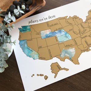 May include: A gold and blue watercolor map of the United States with the text "places we've been" at the top. Each state is outlined in gold and filled with a watercolor wash in shades of blue and gold.