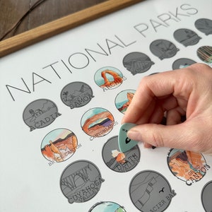 May include: A white poster with the title "National Parks" printed at the top. The poster features a grid of illustrated national parks, including Acadia, Arches, Bryce Canyon, Canyonlands, Cuyahoga Valley, Death Valley, Glacier Bay, Grand Canyon, and more. Each park is represented by a circular icon with a unique illustration.