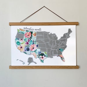 May include: A framed map of the United States with a floral design overlay. The map is gray with state borders and names. The floral design is in shades of pink, purple, blue, and green. The text "adventure awaits" is at the top of the map.