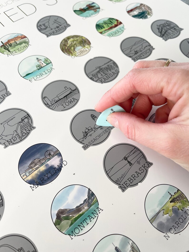 May include: A scratch-off map of the United States with illustrations of each state. The map features a hand holding a tool to scratch off the foil layer of the Massachusetts state illustration. The map includes state names and illustrations.